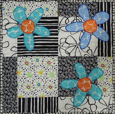 A table topper in black & white with three flowers in teal and blue