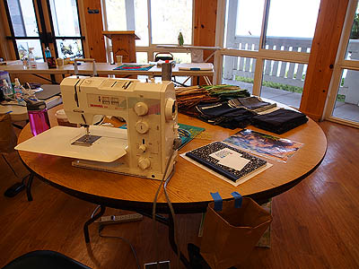 Table with sewing machine and fabric in front of large windows