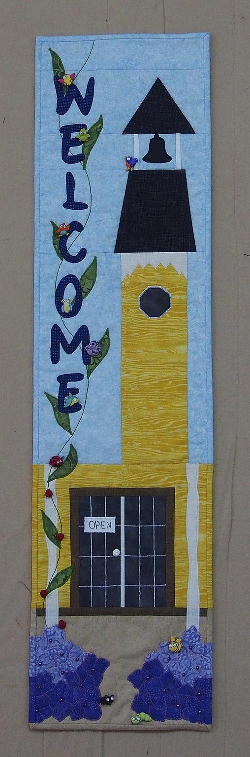 Quilted depiction of the quilts shop Country Concessions with a yellow building & bell tower
