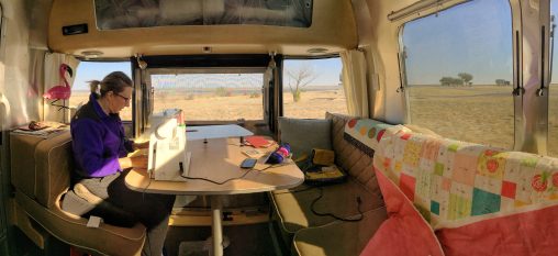 Jen sitting at the table in our 27FB Eddie Bauer Airstream working on quilts with Texas scenery seen through the windows.