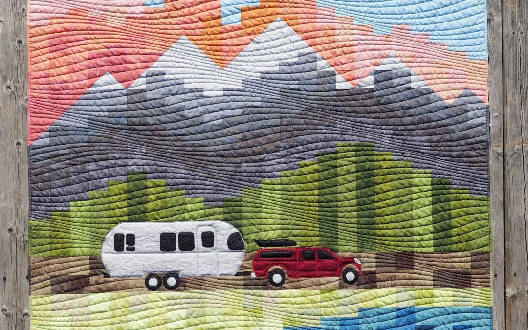 Custom airstream quilt showing an airstream being towed across a landscape of river mountains and sunset