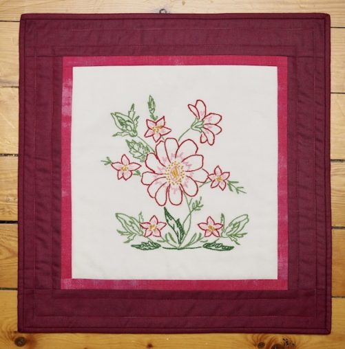 Burgundy border frames this embroidered pink flower