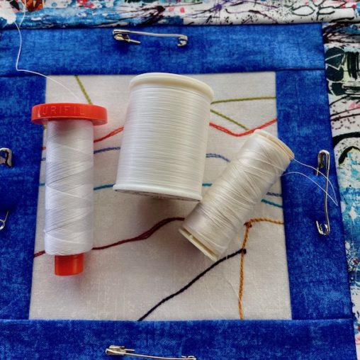 3 different sized spools of white thread on a white and blue block