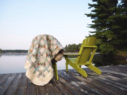 two chairs on a dock with a quilt draped over one