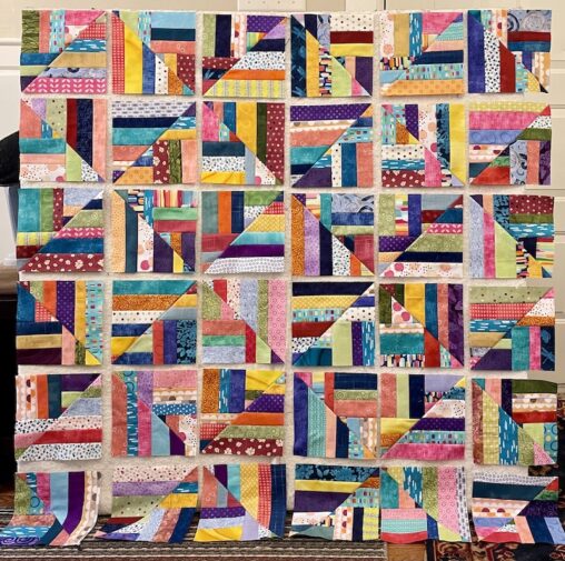 multiple colours of fabric strips make up many quilt blocks on a design wall